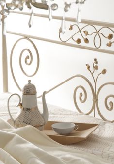 a tea pot and saucer sitting on a tray in front of a white iron bed