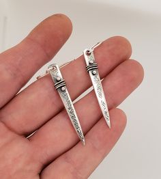 a pair of silver earrings that are on someone's hand