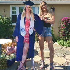 two women standing in front of a house wearing graduation caps and gowns, posing for the camera