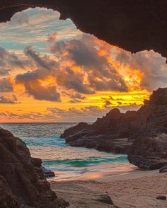 the sun is setting over the ocean from inside a cave on the beach with rocks and sand