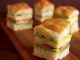 small sandwiches stacked on top of each other on a cutting board with one cut in half