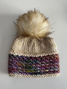 a knitted hat with a fur pom on the top and multicolored yarn