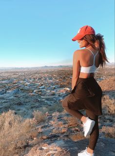 a woman standing on top of a rocky hillside wearing a red hat and brown pants