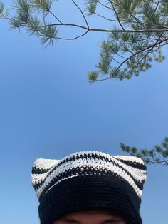 a young boy wearing a knitted hat under a pine tree with blue sky in the background