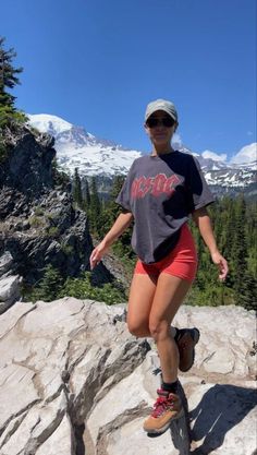 a woman on a skateboard jumping over some rocks in front of snow capped mountains