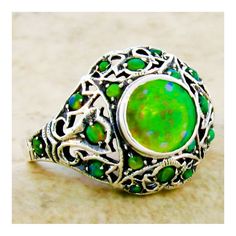 This exquisite piece is a Vintage Estate ring, featuring a green lab-created fire opal as its centerpiece, set within an intricate filigree design. Complementing the central stone are green lab-created opal accent stones, adding to the ring's overall allure. The ring is crafted from 925 solid sterling silver, ensuring both quality and durability. The dimensions of the ring are noteworthy, with the top measuring just over 1/2 inch in length, providing a substantial and elegant presence on the fin Vintage Green Opal Round Ring, Green Cabochon Opal Ring, Green Opal Birthstone Jewelry, Green Opal May Birthstone Ring, Formal Green Hallmarked Opal Ring, Green Gemstone Filigree Ring For May Birthstone, Green Opal Ring For May Birthstone, Green Opal Round Ring For May Birthstone, Green Opal Cabochon Ring