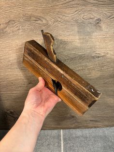 a hand holding a wooden object on top of a tile floor next to a wall