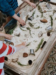 two children playing with sand and seashells on a table in front of a mirror