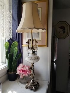 a lamp on a table next to a potted plant and a cactus in a vase