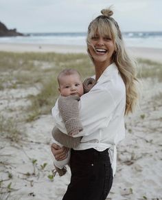 a woman holding a baby in her arms on the beach