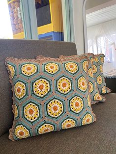 two crocheted pillows sitting on top of a gray couch next to a window