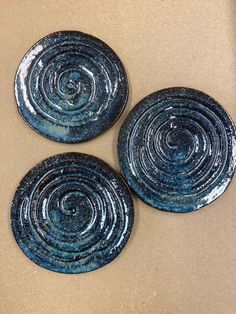 three blue plates sitting on top of a brown table next to each other and one has swirl designs on it