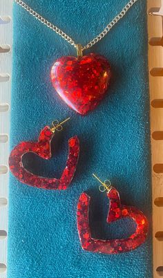 Standout with this vibrant red heart pendant and open heart post back earrings. 18" gold nickle free iron curb chain, 2mm. Lobster clasp closure. Earrings have gold hypoallergenci posts. Made with epoxy resin and red chunk glitter. Handcrafted items often have slight imperfections which are part of the creative process and add to the character of the piece; no 2 are alike!  Colors you see on the screen may differ slightly from in person due to variations in lighting, camera and electronic postin Red Heart Pendant Earrings, Red Heart Print Earrings For Gifts, Trendy Red Heart Earrings For Gift, Heart Shaped Resin Jewelry For Party, Trendy Resin Jewelry For Valentine's Day, Red Double Heart Pierced Jewelry, Trendy Red Heart-shaped Jewelry, Red Pierced Heart Earrings As Gift, Valentine's Day Resin Jewelry With Heart Charm