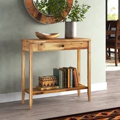 a wooden table with books and a plant on it next to a wall mounted mirror