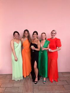 four women standing next to each other in front of a pink wall holding wine glasses