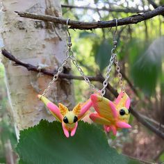 two yellow and pink flowers hanging from chains on a tree branch in the woods,