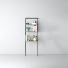 a shelf with books and vases on it in an empty room next to a white wall