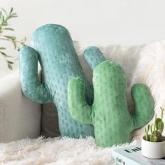 a green cactus pillow sitting on top of a white couch next to a potted plant