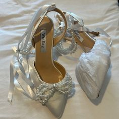 a pair of white high heeled shoes with pearls on the side and a satin bag next to them