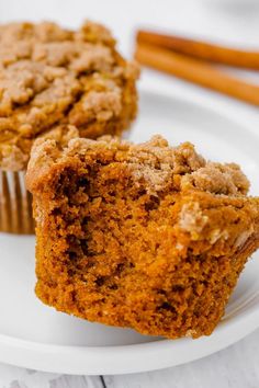 two muffins sitting on top of a white plate next to cinnamon sticks and a cupcake