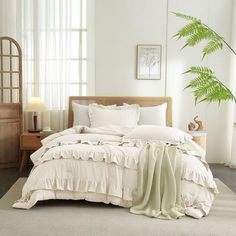 a bed with white sheets and pillows next to a large green plant in a room