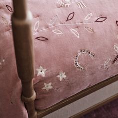 a close up of a bed with pink linens and embroidered designs on the sheets