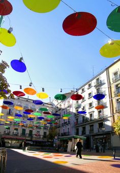 many multicolored umbrellas are hanging in the air above a city street with buildings