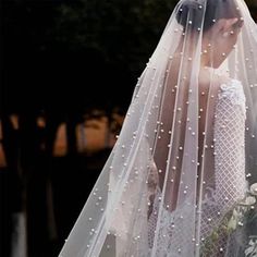 the bride is walking down the street in her wedding dress and veil with pearls on it