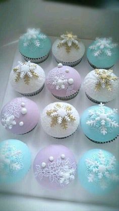 twelve cupcakes decorated with frosting and snowflakes are in a box