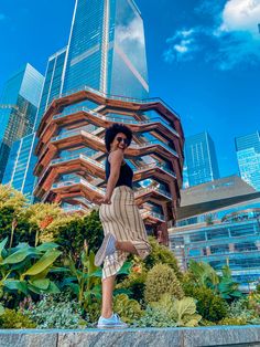 a woman standing in front of a tall building with her legs spread out and wearing sunglasses