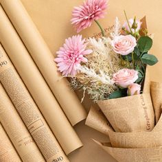 pink flowers are in a vase on top of an old book and some rolled up papers