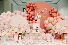 a table topped with pink and white desserts next to balloon wall covered in balloons