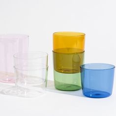 four different colored glass cups sitting next to each other on a white surface, with one empty cup in the middle