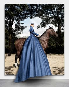 a woman in a blue dress riding a horse