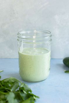 a glass jar filled with green liquid next to some greens on a blue counter top