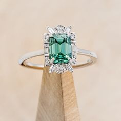 Product Details Ring Style: The "Cleopatra" is an emerald-cut green moissanite women's engagement ring with diamond accents. Many other center stone options are available upon request. Center Stone: 8x6mm Emerald-Cut Green Moissanite Materials: 14K gold engagement ring featuring a green moissanite center stone and 1/5 CTW accent diamonds Customizable: Basic customizations can be accommodated by simply adding a request in the “Custom Requests” section during checkout. A common example is to request a darker-colored stone of the same material. For more extensive customizations, such as stone swaps, please contact us! We would be honored to make your ring even more meaningful! Available In: 14K White Gold, 14K Yellow Gold, or 14K Rose Gold Dreaming Bigger? Because each ring is handcrafted to Green Moissanite Engagement Ring, Green Moissanite, Staghead Designs, Colored Stone, Ring With Diamond, Ceramic Rings, Montana Sapphire, Detailed Ring, Tungsten Ring