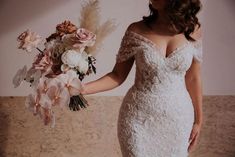 a woman in a wedding dress holding a bridal bouquet with flowers on the side