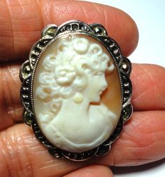 Cameo brooch pin is a Vintage antique Italian cameo pin in a solid sterling silver frame with marcasites on the mounting. Genuine vintage carved shell cameo in solid sterling silver frame mounting with marcasites adding sparkle and embellishing the ornate cameo frame. This lovely vintage cameo treasure, is a a genuine hand carved shell cameo, and it can be worn as a brooch or pendant. The cameo is signed by the artist on the back. There is a loop for a chain or ribbon on the back. The back frame Antique Carved Brooches For Weddings, Antique Cameo Brooches For Wedding, Ornate Carved Oval Brooches, Ornate Oval Carved Brooches, Victorian White Cabochon Brooches, White Victorian Cabochon Brooches, White Cameo Brooch For Wedding, White Oval Cameo Brooches, White Cameo Brooches For Wedding