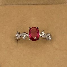 a ring with a red stone and two white diamonds on it in a cardboard box