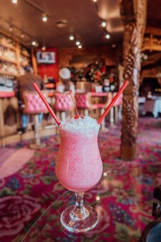 a pink drink sitting on top of a glass table in a room filled with tables and chairs