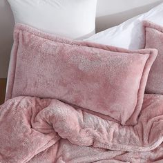 a bed with pink comforter and pillows on top of it, next to a white pillow