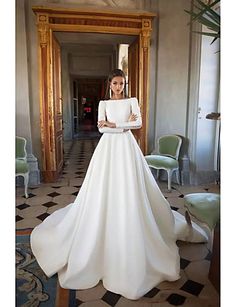 a woman in a white wedding dress standing next to a chair with her arms crossed