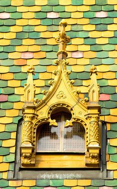 an ornate gold window on the side of a colorful brick building with green and yellow shingles