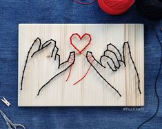 two hands holding a heart on a piece of wood with yarn next to it and scissors