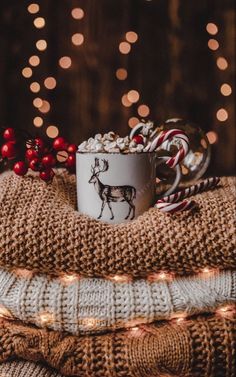 a coffee cup with marshmallows and candy canes on it sitting on a blanket