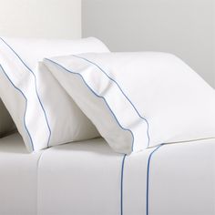 two white pillows with blue piping on them next to each other in a bed