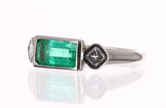 A Colombian emerald and princess cut three stone ring. Dexterously handcrafted in gleaming 18K white gold, this ring features a 1.40-carat natural elongated emerald, emerald cut from the famous Muzo mines. Set in a secure bezel setting for extra protection. This extraordinary emerald has stunning bluish-green color and an incandescent glow. The emerald has beautiful clarity with natural Jardins that occur in all earth mined emeralds. Bezel set, princess cut diamonds accent the center gem. This r Three Stone Rectangular Diamond Jewelry, Rectangular Three Stone Diamond Jewelry, White Gold Three Stone Rectangular Jewelry, Rectangular Three Stone White Gold Jewelry, Fine Jewelry With Three Stone Rectangular Design, Fine Jewelry Rectangular Three Stone, Fine Jewelry Rectangular Three-stone, Elegant Rectangular Three-stone Jewelry, Multi-stone Platinum Jewelry With Emerald Cut