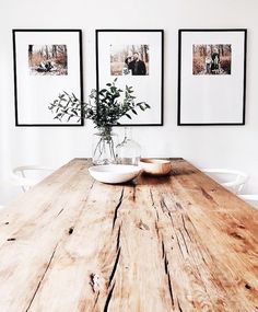 a wooden table topped with two white bowls filled with flowers next to pictures on the wall