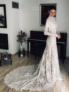 a woman standing in front of a piano wearing a long sleeved wedding dress with high neck