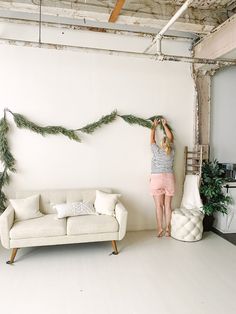 a woman standing on top of a couch next to a white sofa in a living room